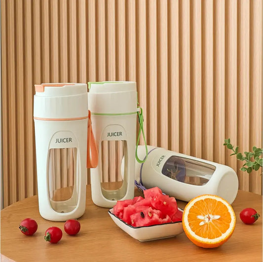 Two portable juicers on a wooden table with fruits and a plant in the background.